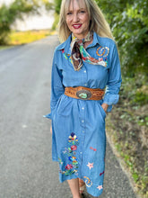 Woman wearing a blue embroidered dress with a decorative belt on a road.