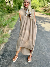 Woman in a beige dress standing on a road with greenery in the background