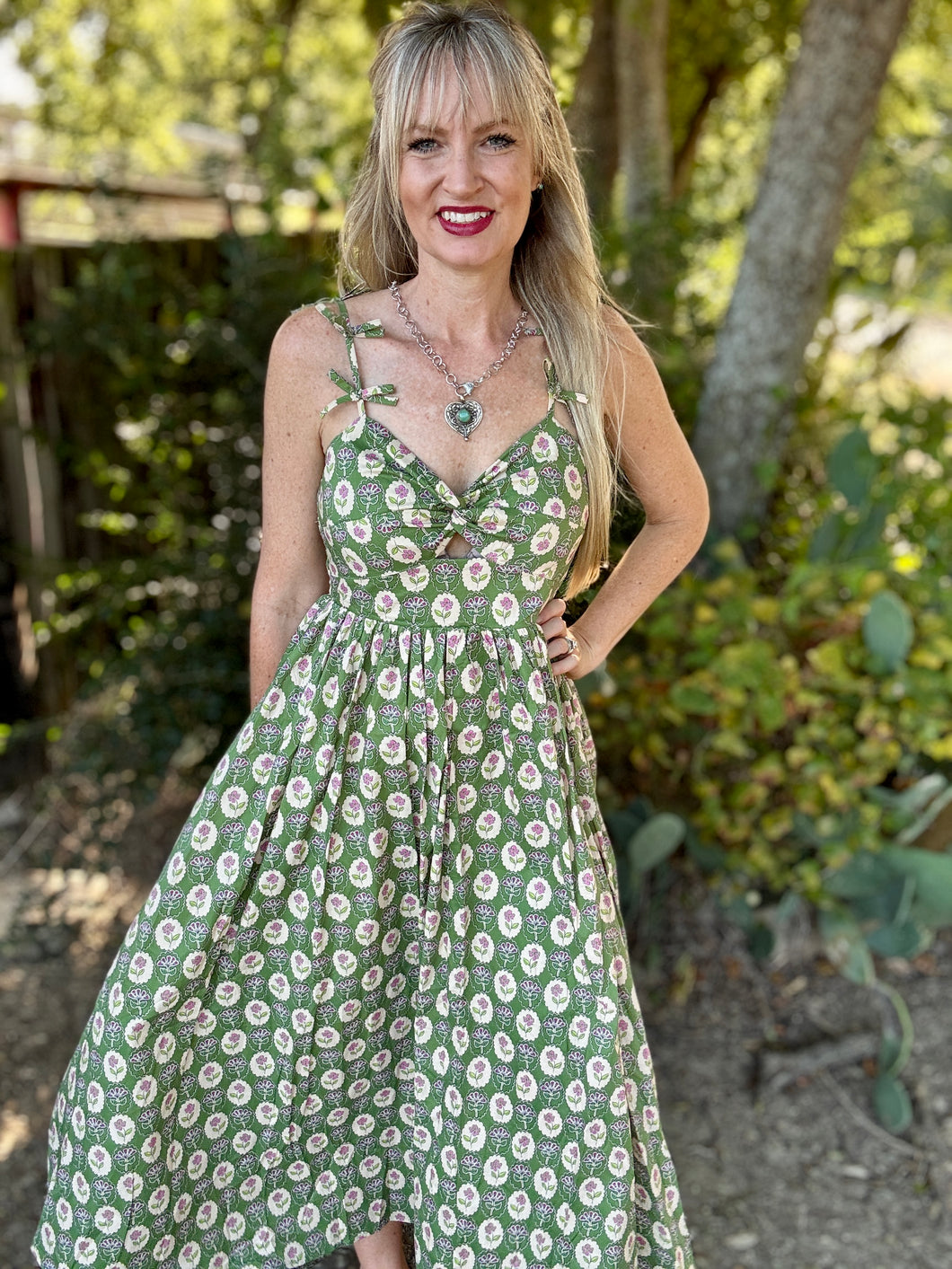 Woman wearing a green floral dress standing outdoors with trees in the background