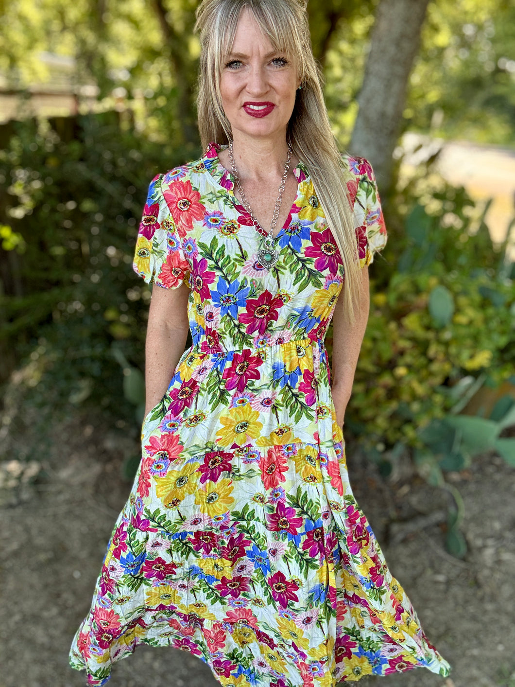 Woman wearing a colorful floral dress standing outdoors with greenery in the background