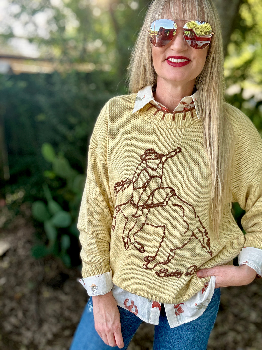 Woman wearing a yellow sweater with a horse design outdoors