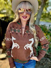 Woman wearing a brown sweater with horse designs, sunglasses, and a cowboy hat outdoors.