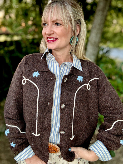Woman wearing a brown embroidered sweater with a striped shirt outdoors