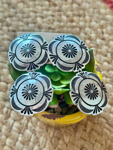 Decorative concho earrings with floral designs on a textured surface