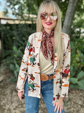 Woman wearing a patterned blazer with a bandana, sunglasses, and jeans outdoors.