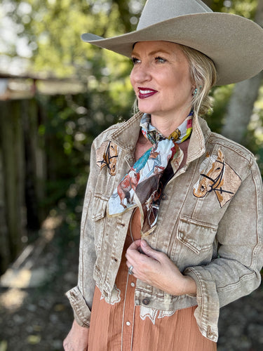 Woman wearing a beige cowboy hat and jacket with horse designs outdoors.
