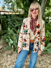 Person wearing a patterned shirt with cowboy graphics, sunglasses, and a scarf outdoors.