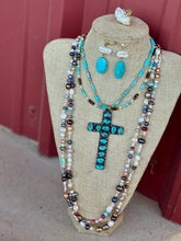 Jewelry set with cross pendant on a beige display bust against a red background