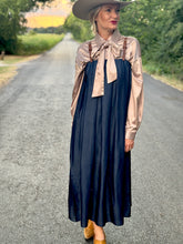 Woman in a navy dress with a beige blouse and wide-brimmed hat standing on a rural road.