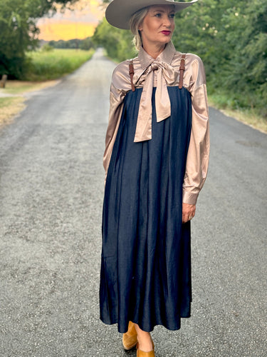 Woman in a navy dress with a beige blouse and wide-brimmed hat standing on a rural road.