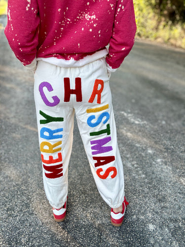 Person wearing a red long-sleeve shirt and white sweatpants with 'Merry Christmas' in colorful letters on a road.