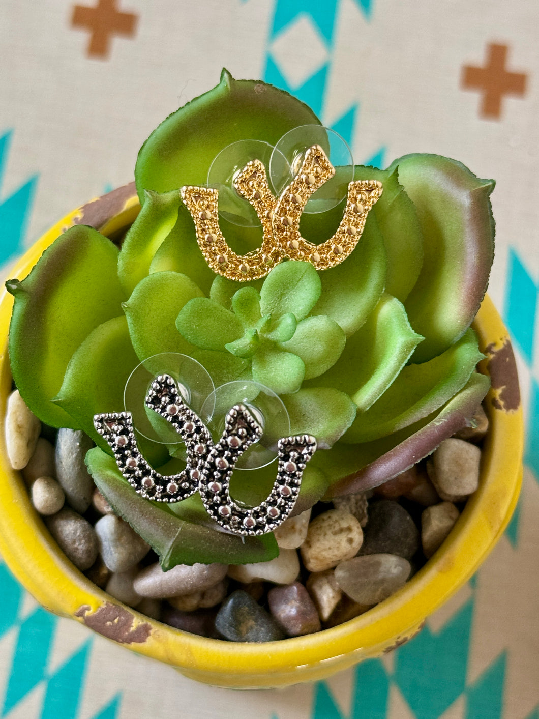 Gold and silver horseshoe earrings on a succulent plant with pebbles.