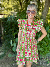 Woman wearing a green floral dress with sunglasses and red lipstick, standing in a garden.