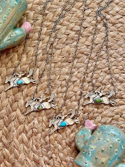 Silver necklaces with bucking horse pendants on a woven surface
