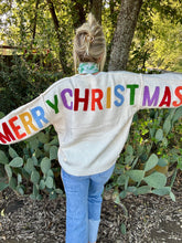 Person wearing a sweater with 'Merry Christmas' in colorful letters outdoors.