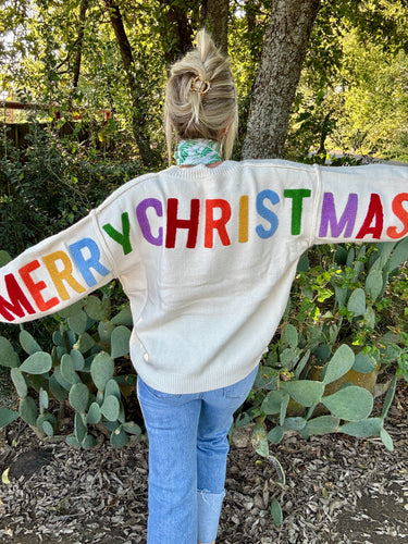 Person wearing a sweater with 'Merry Christmas' in colorful letters outdoors.