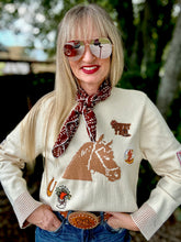 Woman wearing a sweater with horse designs and a scarf, outdoors.