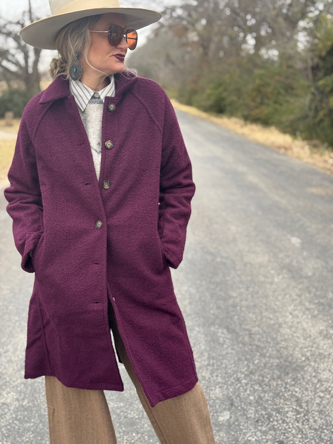 Person wearing a purple coat and hat on a road with trees in the background