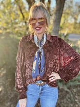 Woman wearing a patterned blouse, blue jeans, and sunglasses with a blurred natural background