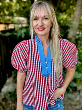 Woman wearing a red and white checkered blouse with blue trim outdoors.