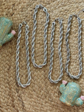 Silver chain necklace on a textured woven surface with decorative shells.