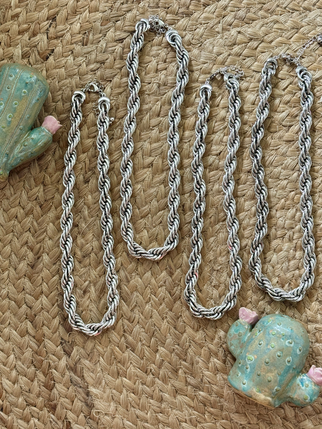 Silver chain necklace on a textured woven surface with decorative shells.