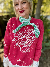 Person wearing a red 'Holly Jolly' sweater with a green and white scarf outdoors.