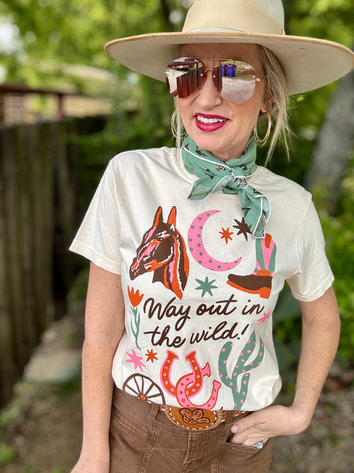 Person wearing a white t-shirt with a graphic design and text, sunglasses, and a hat outdoors.