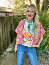Woman wearing a pink floral jacket, colorful shirt, and blue jeans outdoors.