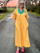 Woman in a yellow striped dress standing on a road with a sunset in the background