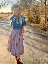 Woman in a blue top and plaid skirt standing on a rural road.