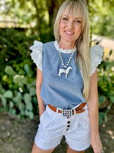Woman wearing a blue top with ruffled sleeves and white shorts outdoors.