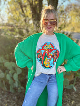 Woman wearing a green cardigan, graphic t-shirt, and sunglasses outdoors.