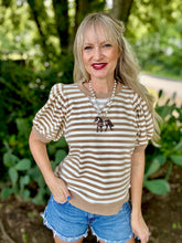 Woman wearing a striped shirt and denim shorts outdoors with greenery in the background