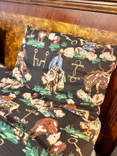 A close-up of a bed featuring a western-themed bedding set with a black background and a detailed print of a cowboy, lasso, boots, horseshoes, and cattle, set against a dark wood headboard.