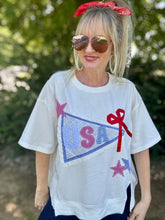 Woman wearing a white t-shirt with 'USA' and star designs outdoors.