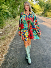 Woman in a colorful dress with patterns walking on a road surrounded by greenery.