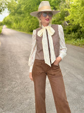 Woman in vintage-style outfit with hat and scarf standing on a road.