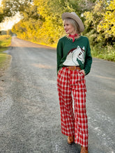 Woman in a green sweater with a horse design and red plaid pants standing on a road.
