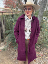 Person wearing a purple coat, beige hat, and patterned sweater outdoors.