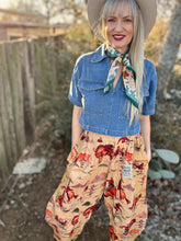 Woman wearing a denim shirt, western pants, and a wide-brimmed hat outdoors.