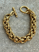 A chunky gold-toned chain bracelet with a toggle clasp, photographed on a textured gray stone surface.