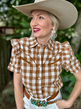 Woman wearing a brown and white checkered shirt with a cowboy hat and turquoise belt buckle.