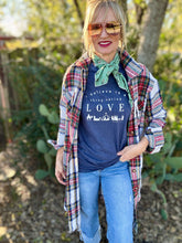 Woman wearing a navy t-shirt with 'I believe in things called love' text, plaid shirt, and sunglasses outdoors.