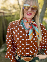 Woman wearing a brown polka dot blouse with a colorful scarf, sunglasses, and a belt with a large buckle.