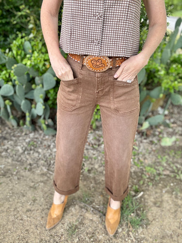 Person wearing brown pants and a checkered shirt with a belt buckle, standing in front of cacti.