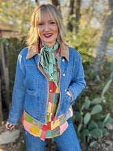 Woman wearing a denim jacket and colorful shirt outdoors with greenery in the background