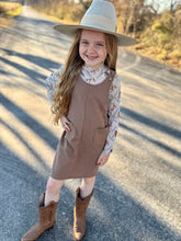 Young girl in a brown dress and hat standing on a road
