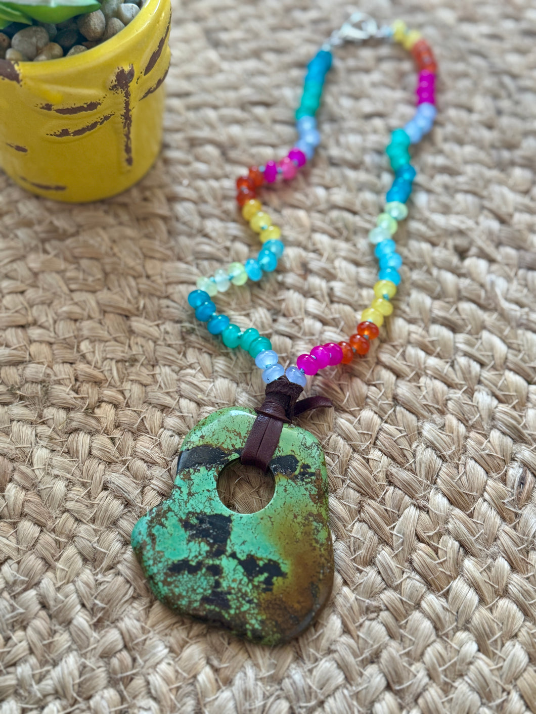 Colorful beaded necklace with a green stone pendant on a woven surface
