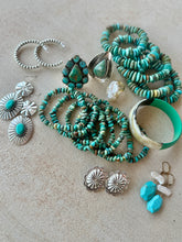 Collection of turquoise and silver jewelry on a beige surface